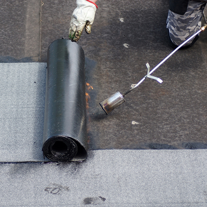 Flat roof installation with propane blowtorch during construction works with roofing felt